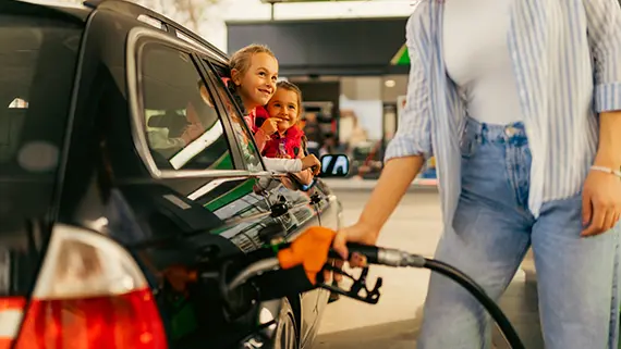 Deux enfants regardent leur mère faire le plein d’essence dans leur voiture.