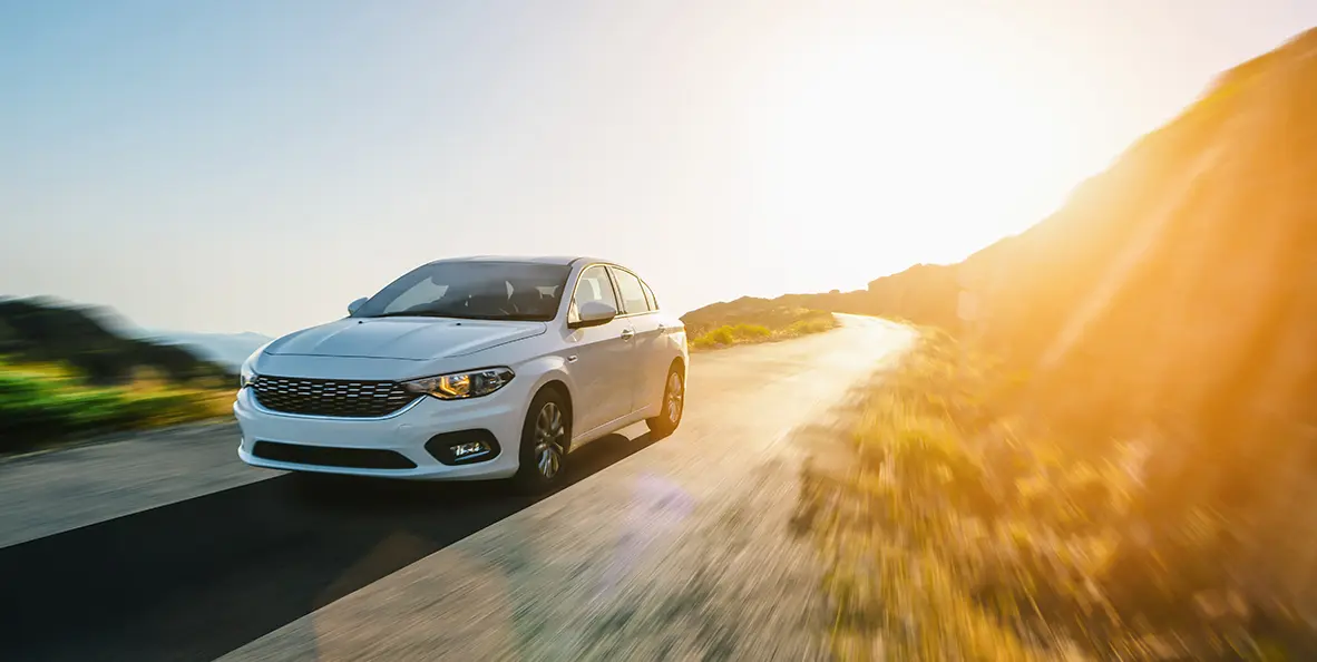 Véhicule blanc circulant sur une route à côté d'une colline.